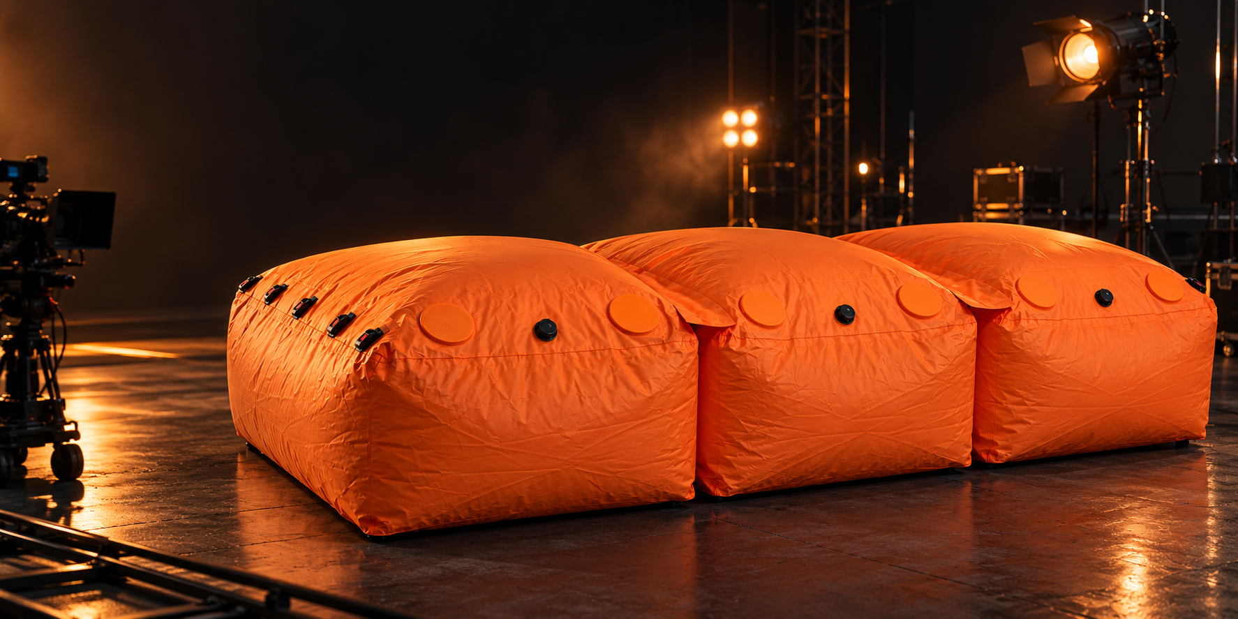 Orange modular inflatable landing system on a film soundstage, with camera equipment and stage lighting nearby